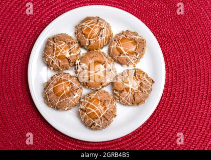 Sept biscuits bruns aux noisettes et aux cacahuètes cassants sur une assiette brune transparente, crème caramel. Plaque blanche sur fond rouge Banque D'Images