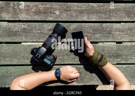 Homme tenant un smartphone et un appareil photo reflex numérique Banque D'Images