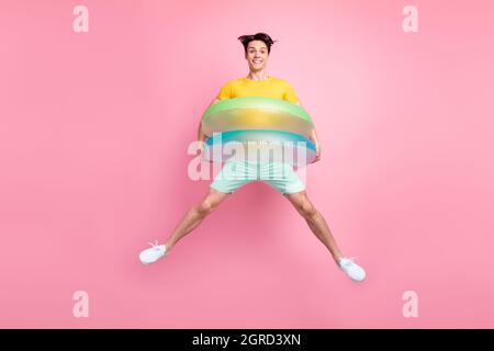 Photo de gentil puéril gars saut couverture corps deux cercles en caoutchouc porter un t-shirt jaune short isolé sur fond rose Banque D'Images