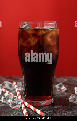 Verre de cola, glace et pailles sur fond rouge. Banque D'Images