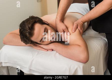 Masseuse effectuant un massage des épaules à un jeune homme dans le centre de spa Banque D'Images