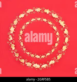 Double couronne de Noël décorative abstraite avec feuilles de houx dorées et étoiles sur fond rouge. Symbole de fête pour Noël et le nouvel an Banque D'Images