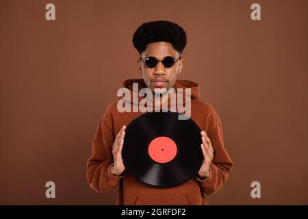 Photo du jeune homme africain tenir rétro disque vinyle assiette musique hipster lunettes isolées sur fond brun de couleur Banque D'Images