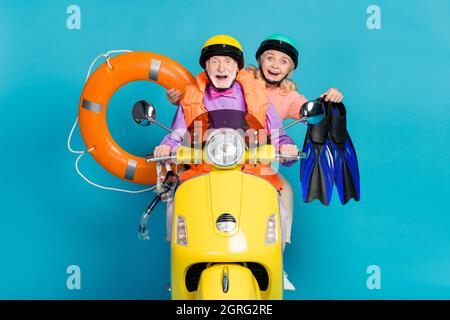 Photo de gris cheveux mariés retraités retraités couple tenir anneau gonflable vacances vélo casque isolé sur fond bleu couleur Banque D'Images