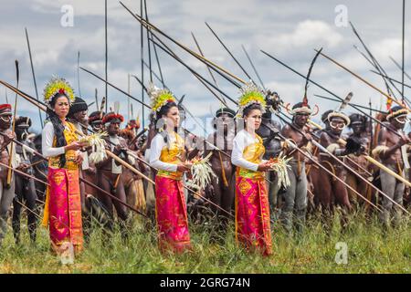 Indonésie, Papouasie, ville de Wamena, femmes balinaises en robe traditionnelle apportant une touche de culture nationale lors d'une reconstitution de scène de guerre tribale, par des hommes armés de la tribu Dani. Festival culturel de Baliem Valley, chaque année en août, les tribus se réunissent pour effectuer des scènes de guerre ancestrales, des défilés et de la danse dans des vêtements traditionnels Banque D'Images