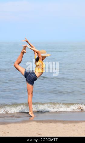 Jeune fille skinny avec chapeau de paille et t-shirt jaune exécute un exercice de gymnastique appelé ECART en été Banque D'Images