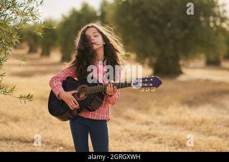 Brunette fille jouant sa guitare avec ses yeux fermés dans une oliveraie au coucher du soleil Banque D'Images