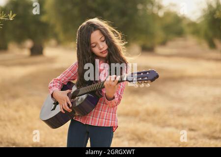 Brunette fille jouant sa guitare dans un champ d'oliviers au coucher du soleil Banque D'Images