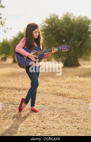 Brunette fille joyeuse jouant sa guitare dans une oliveraie au coucher du soleil Banque D'Images