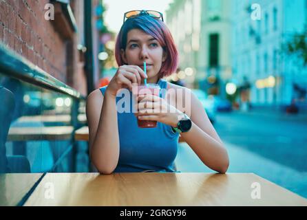 Belle femme aux cheveux brillants assis dans le café de rue et de boire un cocktail en soirée d'été Banque D'Images