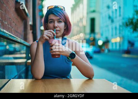 Belle femme aux cheveux brillants assis dans le café de rue et de boire un cocktail en soirée d'été Banque D'Images