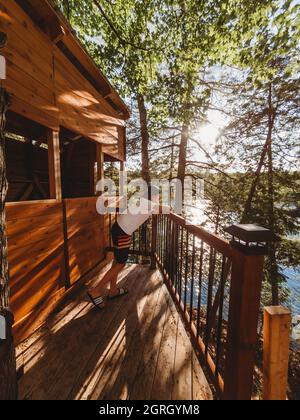 Jeune garçon qui regarde sur le rail d'une maison d'arbres à côté d'un lac. Banque D'Images