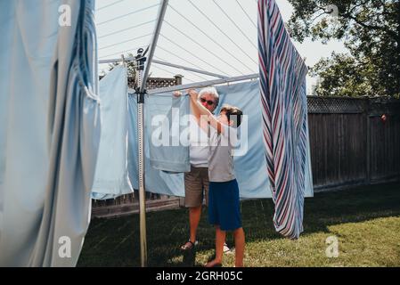 Une femme et un garçon plus âgés qui pendent une buanderie sur une corde à linge extérieure. Banque D'Images