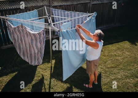 Femme âgée qui pendait une buanderie sur une corde à linge extérieure. Banque D'Images