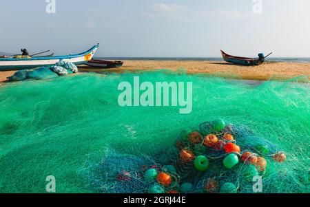 Filet de pêche coloré avec flotteurs sur une plage de sable sous le ciel ensoleillé d'hiver le long de la côte de Coramandel avec des bateaux à Mamallapuram, Tamil Nadu, Inde. Banque D'Images