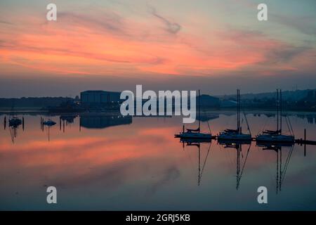 Des yachts à voile amarrés sur un ponton au coucher du soleil dans un port paisible. Banque D'Images