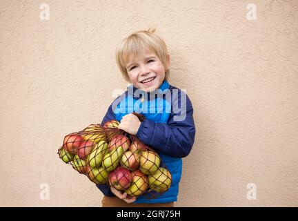 un adorable garçon souriant de 4-5 ans tient devant lui un sac écologique rempli de délicieuses pommes biologiques. Peu d'aide. Délicieux plats végétariens sains. VI Banque D'Images