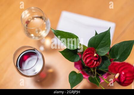 Une belle vue d'une Valentin sur une table en bois, avec des fleurs rouges et des feuilles vertes, à côté d'une note de Valentin et de deux verres de vin. Banque D'Images