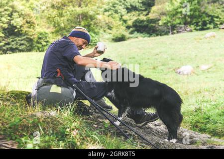 Garçon se reposant sur un rocher après une randonnée en montagne. Homme avec sac à dos buvant une boisson chaude dans une tasse qui regarde la belle nature. Guy extérieur Banque D'Images