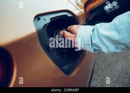 Gros plan de l'homme ouvrant le couvercle du réservoir de carburant de sa voiture pour faire le plein à la station-service. Concept des prix de l'essence Banque D'Images