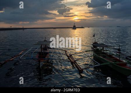 Coucher de soleil avec deux bateaux de pêche en saillie amarrés au Baywalk à Manille, Philippines. Banque D'Images