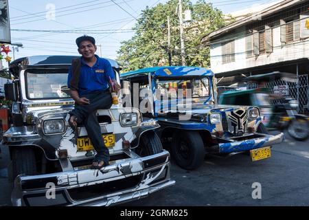 Busdriver prenant une pause est assis sur le capot de sa jeepney. Manille, Philippines. Banque D'Images