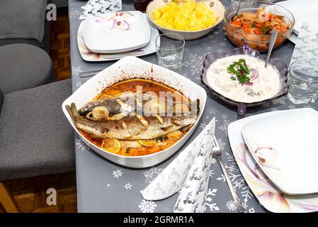 Cuit deux morceaux de truite sur une assiette avec des oignons et des tranches de citron trempées dans l'huile sur la table polonaise de vacances. Banque D'Images