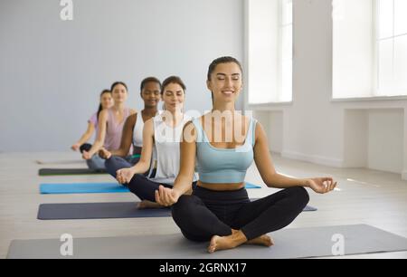 Groupe de femmes détendues heureux ayant cours de yoga à la salle de gym, faisant le lotus poser et méditer Banque D'Images