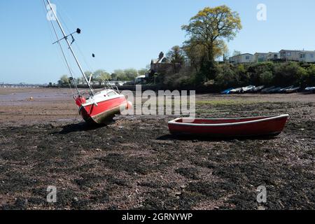 Un petit yacht rouge et un bateau à rames s'agacent à basse eau dans l'estuaire de la rivière Teign près de Teignmouth South Devon England Banque D'Images