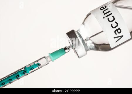 Flacon en verre avec étiquette vaccin sur fond blanc, aiguille de seringue hypodermique verte à l'intérieur - concept de vaccination Banque D'Images