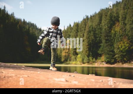 Petit enfant dans une chemise à carreaux et un chapeau gris sur la côte du lac forestier. L'enfance avec la nature aimant concept Banque D'Images