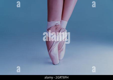 Les pieds de la danseuse de ballet, comment elle pratique les chaussures de pointe s'exerce sur fond bleu. Belles jambes de femme. Ballerine montre classique pas. Banque D'Images