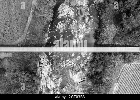 En regardant tout droit sur un pont en béton au-dessus d'une crique rurale bordée de rochers, rendus en noir et blanc Banque D'Images