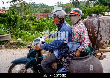 Deux Vietnamiens à bord d'une moto transportant des vases ou des conteneurs à l'arrière. Banque D'Images