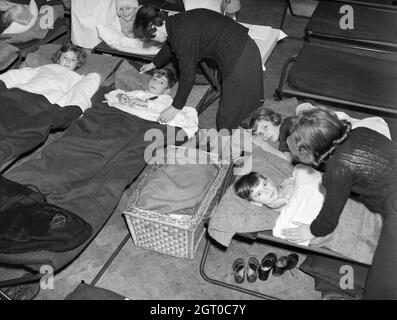 Les sans-abri et/ou les orphelins s'installent pour dormir sur les lits du camp dans le refuge de RAID aérien de l'église John Keble. Un panier au centre de la photo contient probablement un petit bébé, également sans abri par le Blitz. Banque D'Images