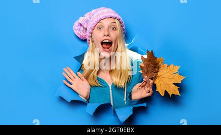 Fille surprise dans un chapeau avec des feuilles d'érable regardant à travers trou de papier. Soldes d'automne. Remise. Ventes saisonnières Banque D'Images