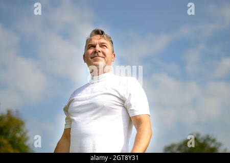 Vue basse contre le ciel d'un homme senior pensif en tenue de sport debout regardant sur le côté avec une expression réfléchie avec l'espace de rédaction Banque D'Images