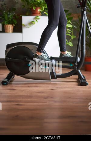 Jambes de femme s'entraîner sur vélo elliptique dans le salon à la maison Banque D'Images