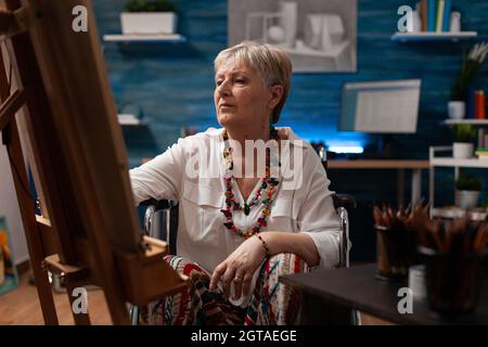 Portrait d'un vieil artiste handicapé assis dans un studio d'art à la maison. Femme aînée avec un handicap en fauteuil roulant se préparant pour le dessin de chef-d'œuvre comme passe-temps. Personne âgée handicapée Banque D'Images