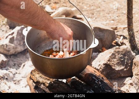 Un homme mélange la soupe à la main dans un chou-fleur. Préparation d'un repas sur feu ouvert Banque D'Images