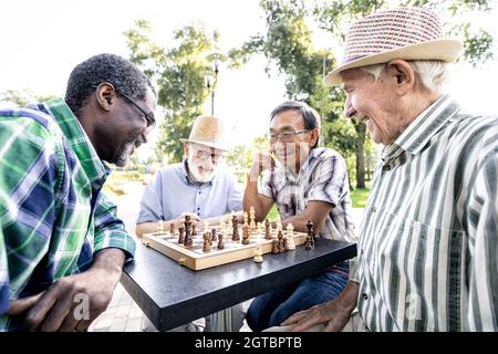 Groupe d'amis seniors jouant au jeu d'échecs au parc. Concepts de style de vie sur l'ancienneté et le troisième âge Banque D'Images