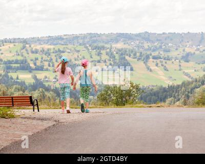 Deux filles explorant, jeunes enfants marchant sur la route ensemble, belle zone rurale, collines, montagnes, campagne paysage pittoresque, heure d'été horizontale Banque D'Images