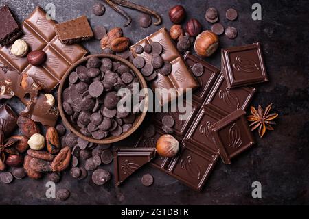 Morceaux de lait savoureux cassé et de barres de chocolat noir avec des gouttes, des fèves de cacao et des noisettes sur fond de méta noir Banque D'Images