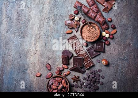 Morceaux de lait savoureux cassé et de barres de chocolat noir avec des gouttes, des fèves de cacao et des noisettes sur fond de béton bleu Banque D'Images