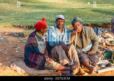 Chencha, Ethiopie - 05 décembre 2013 : soirée sur le marché local. La femme fume un tuyau. Deux femmes et un homme sont assis sur le sol. Banque D'Images