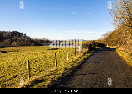 Une route rurale et un lac lors d'une journée d'hiver ensoleillée à Dumfries et Galloway, en Écosse Banque D'Images