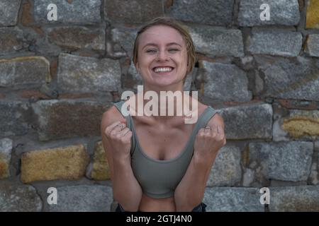 Portrait d'une jeune femme blonde de race blanche heureuse et satisfaite en haut de la récolte sur fond de pierre. Concept des émotions humaines, expression faciale. Amusé Banque D'Images