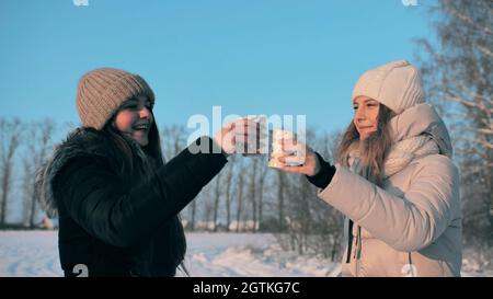 Deux amis boivent du thé chaud en hiver et des verres à clin d'œil embrasent. Banque D'Images