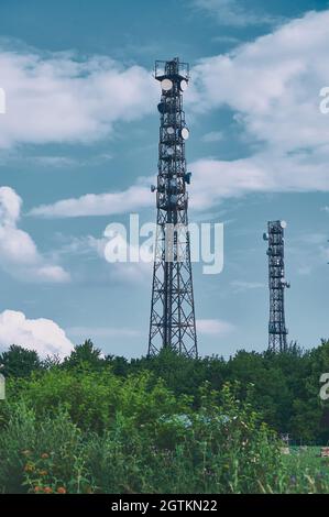 Deux mâts de télécommunications antennes TV technologie sans fil contre ciel bleu sur les bords verts, style couleur froide Banque D'Images