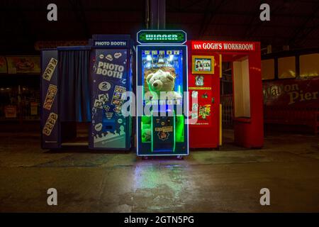 Une machine à griffes avec un signe lumineux lisant Winner tient un grand ours en peluche. L'ours a l'air oublié car il n'y a pas de personnes autour. Banque D'Images